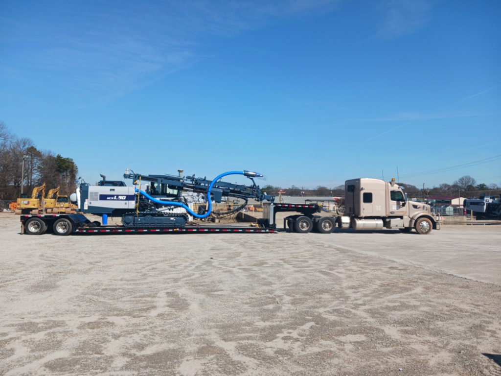 Semi truck hauling an HCR L90 crawler drill rig on a lowboy trailer.