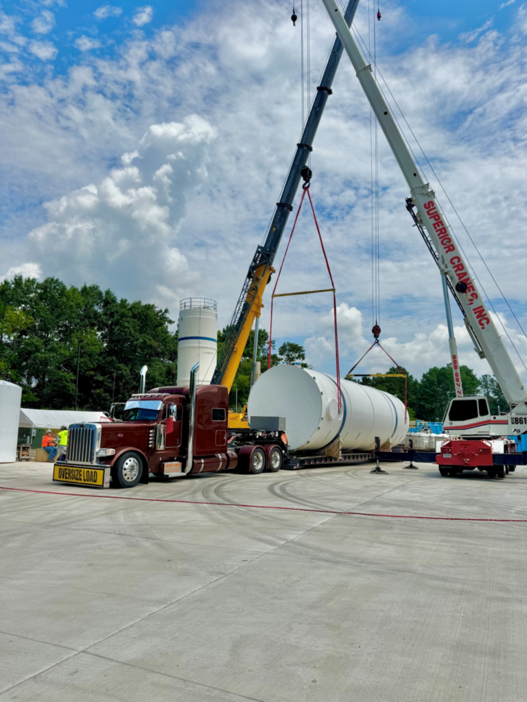 Crane and rigging operation loading a large tank onto a trailer for heavy haul transport.