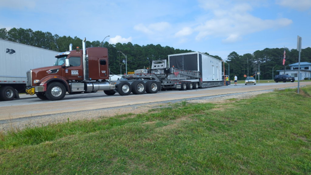 Specialized heavy haul transportation moving a prefabricated modular enclosure for jobsite delivery.